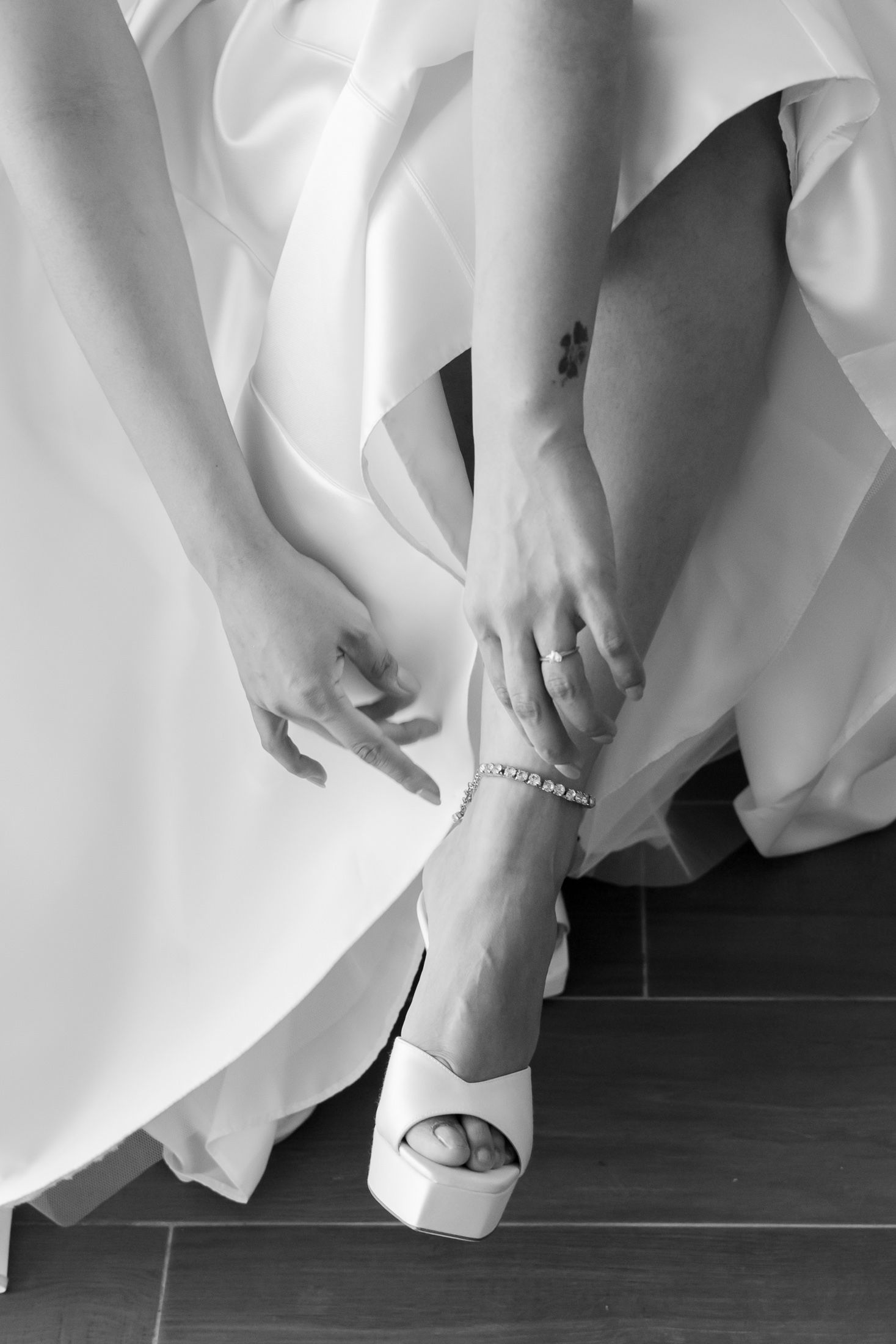 Close-up of bride's feet in elegant white wedding dress against dark floor.
