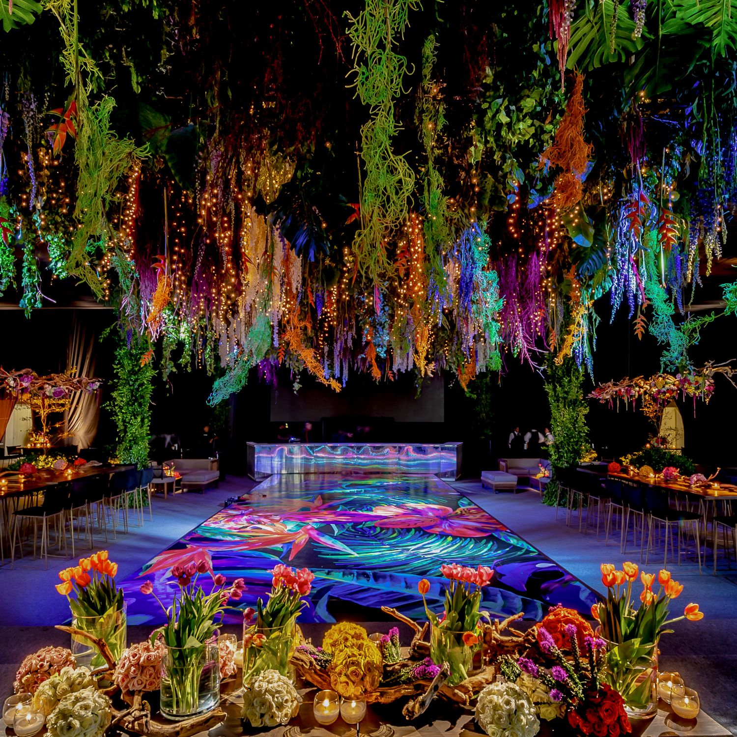 Vibrant floral installation with cascading greenery and colorful lighting creating a magical garden atmosphere.