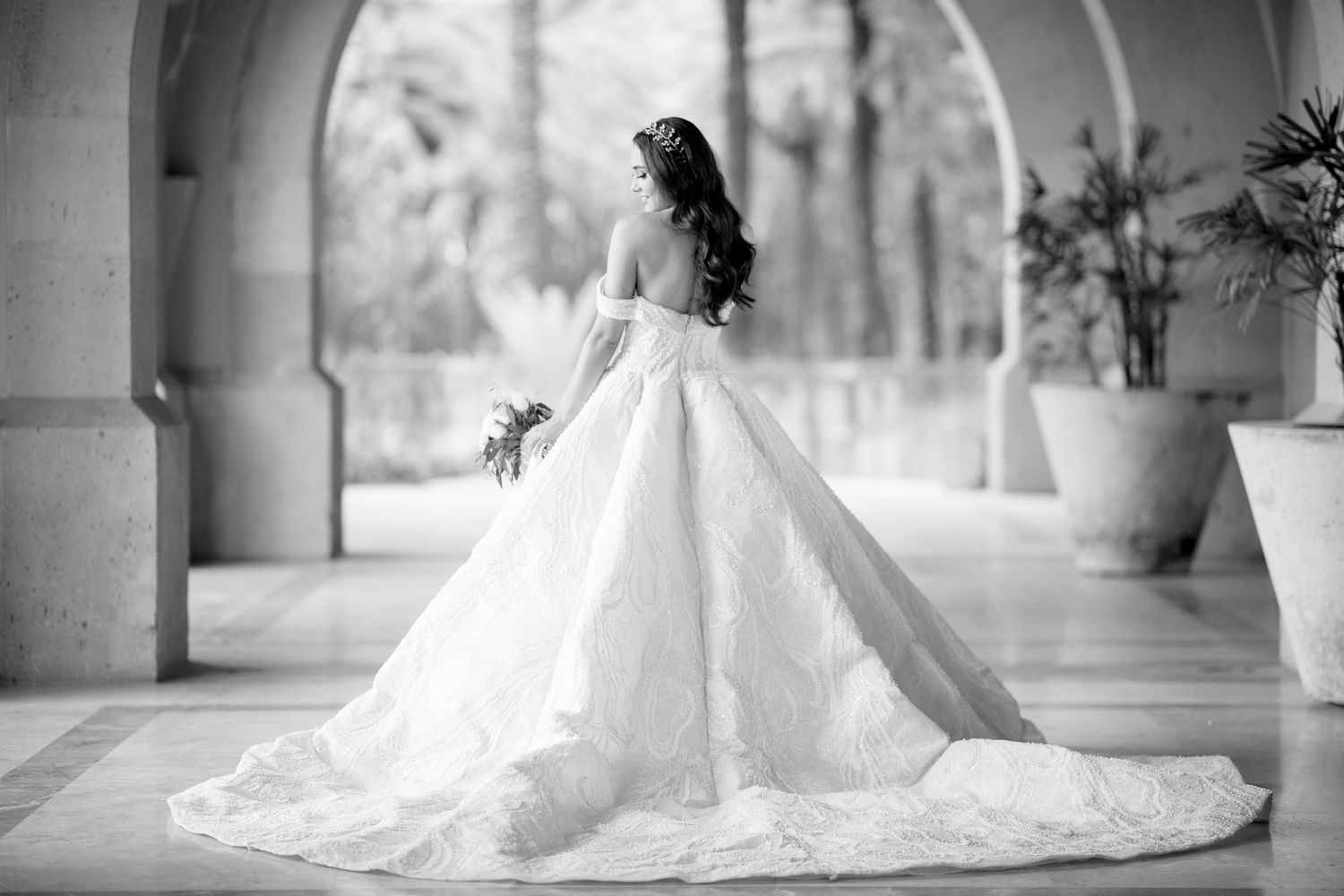 Dramatic black and white photo of a ballgown wedding dress with long train in an arched hallway.
