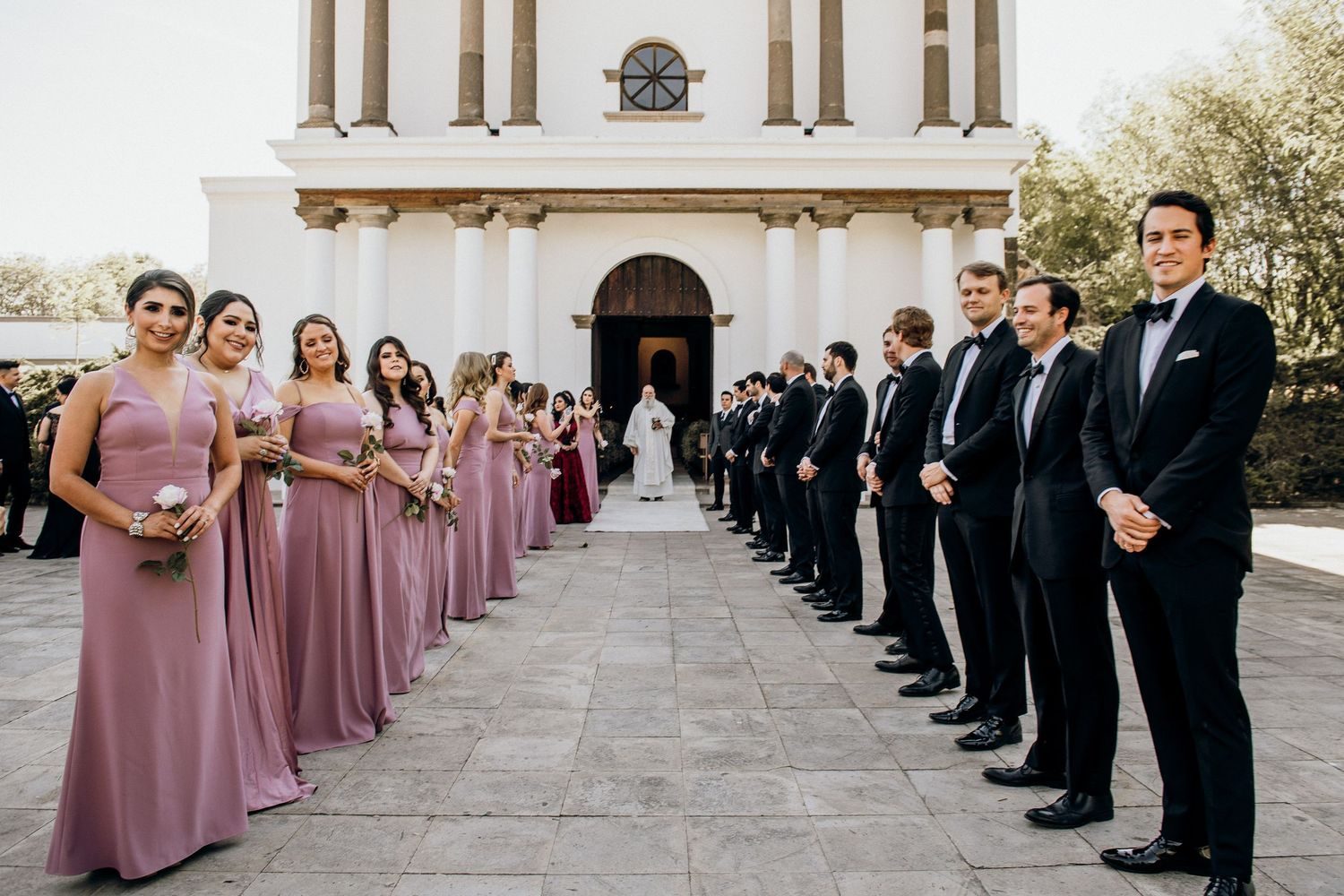 Wedding party lines pathway to church entrance with bridesmaids in pink and groomsmen in black.