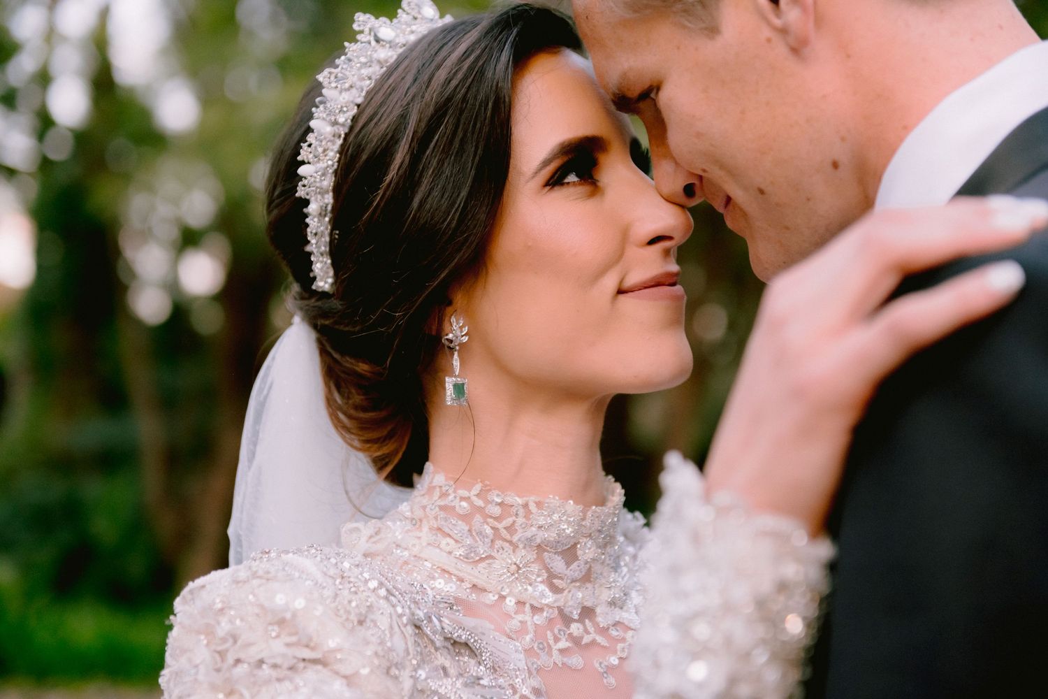 A bride and groom share an intimate moment, the bride wearing a lace gown and crystal tiara with veil.