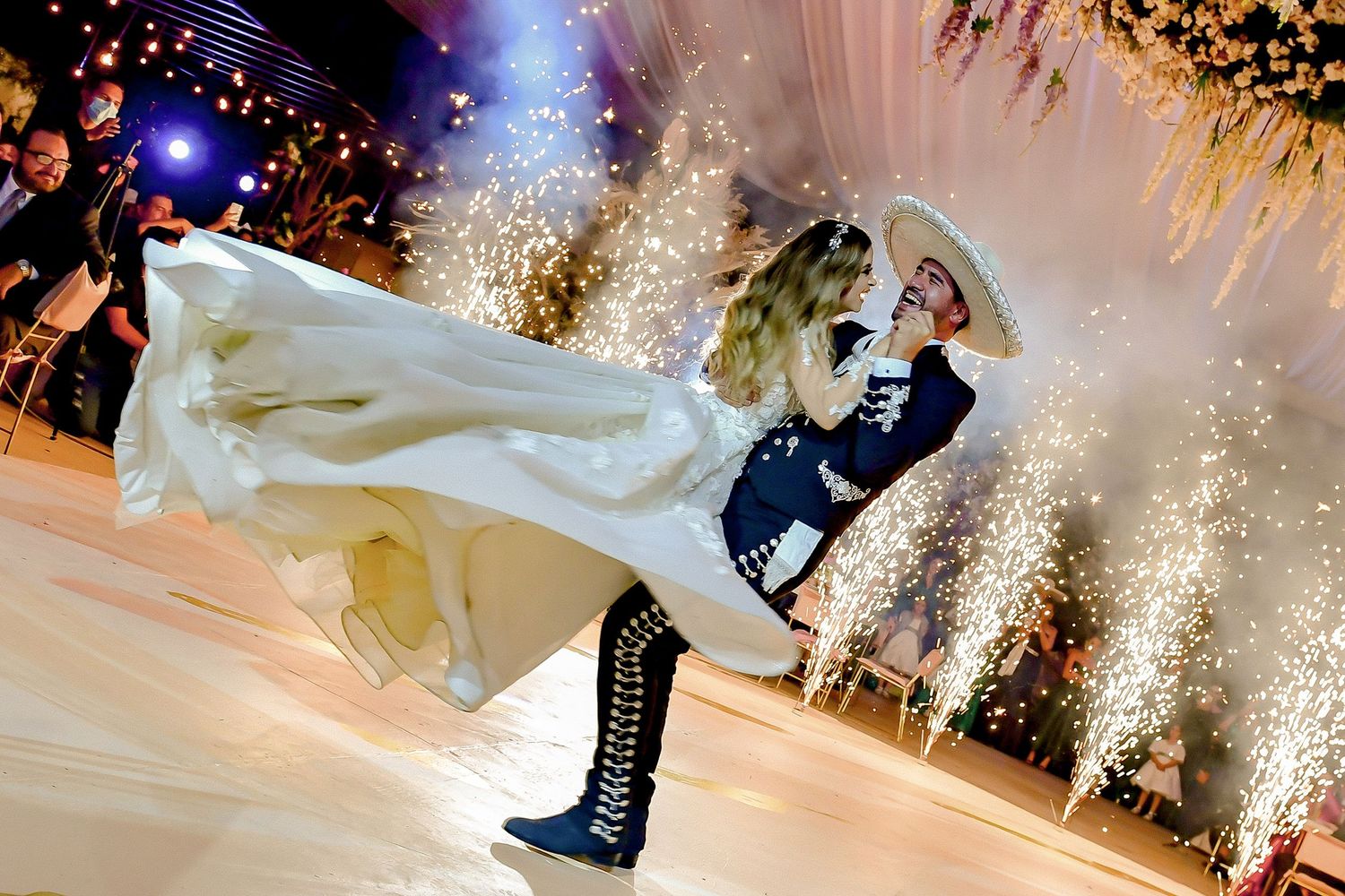 Dramatic sparkler effects illuminate wedding couple's dance on white floor with blue lighting.