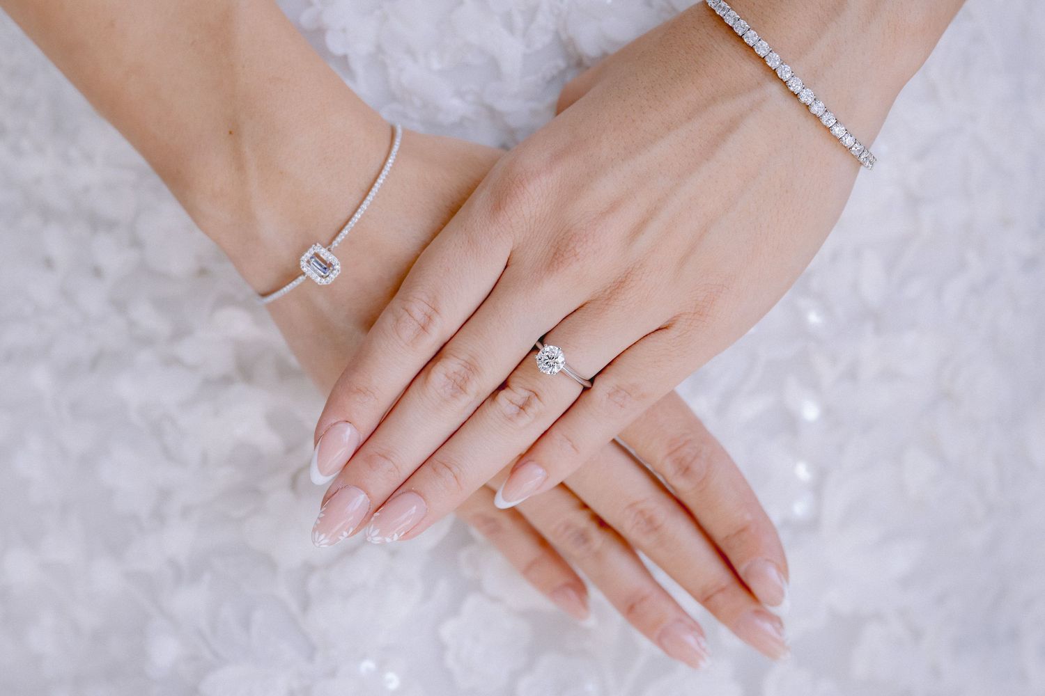Close-up of elegant engagement ring and wedding band on woman's manicured hand against white background.