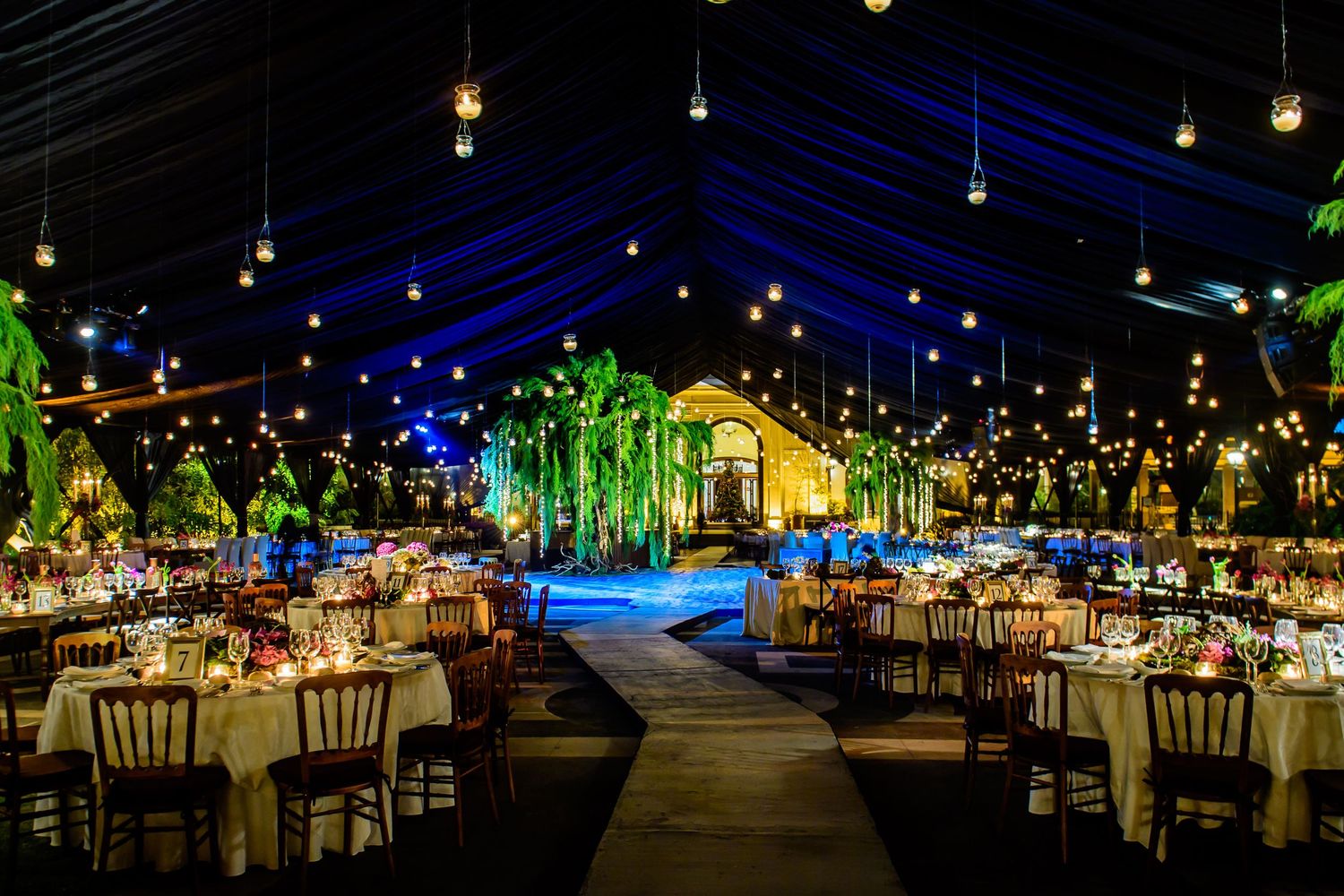 Panoramic view of a luxurious wedding reception space with hanging lights and lush green decor.