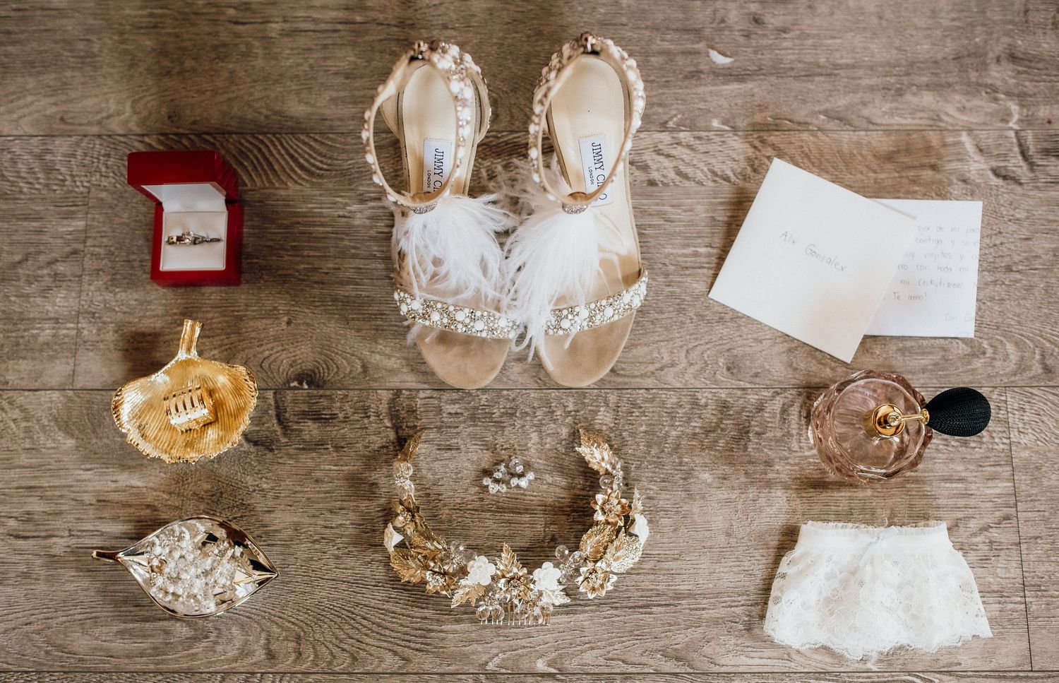 Wedding accessories flatlay including shoes, jewelry, and ring box on wooden surface.