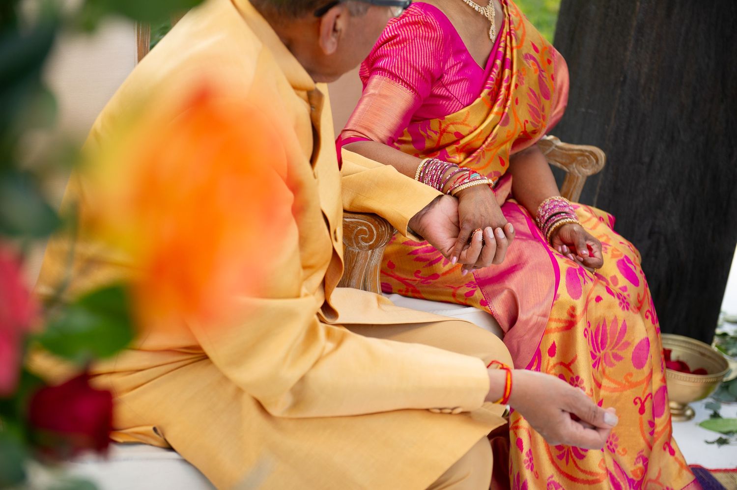 Couple in vibrant Indian wedding attire, bride in pink and orange saree, groom in golden sherwani, holding hands.