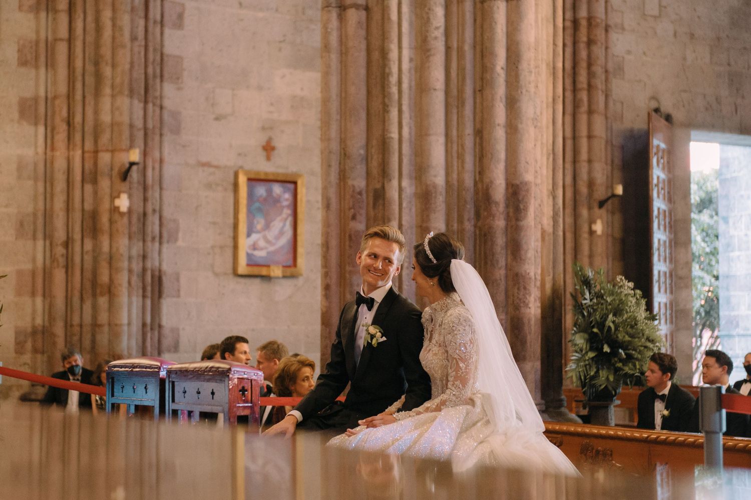 Bride and groom share a tender moment seated inside an ornate church during their wedding ceremony.