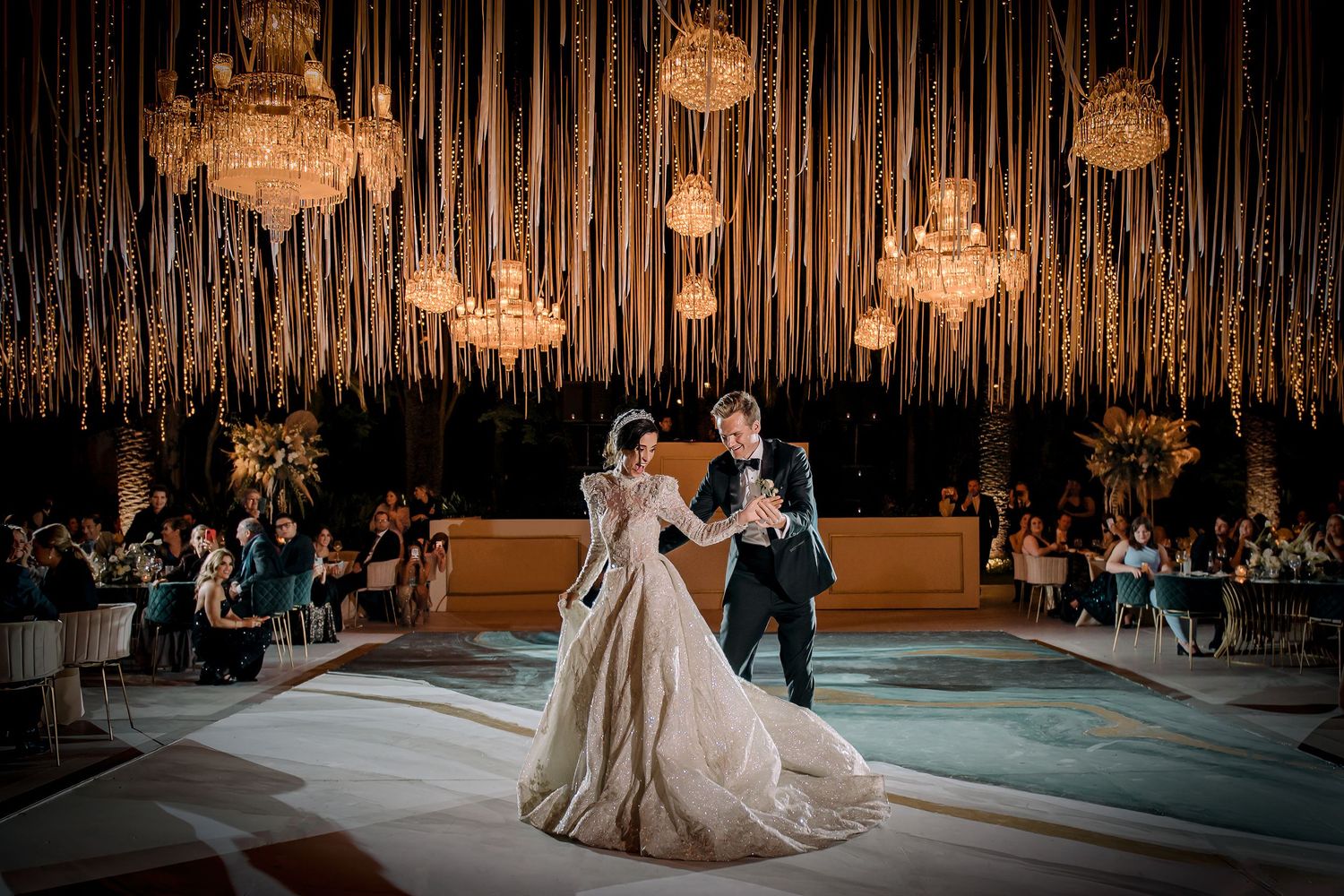Bride and groom share first dance under crystal chandeliers in an elegantly decorated wedding ballroom.