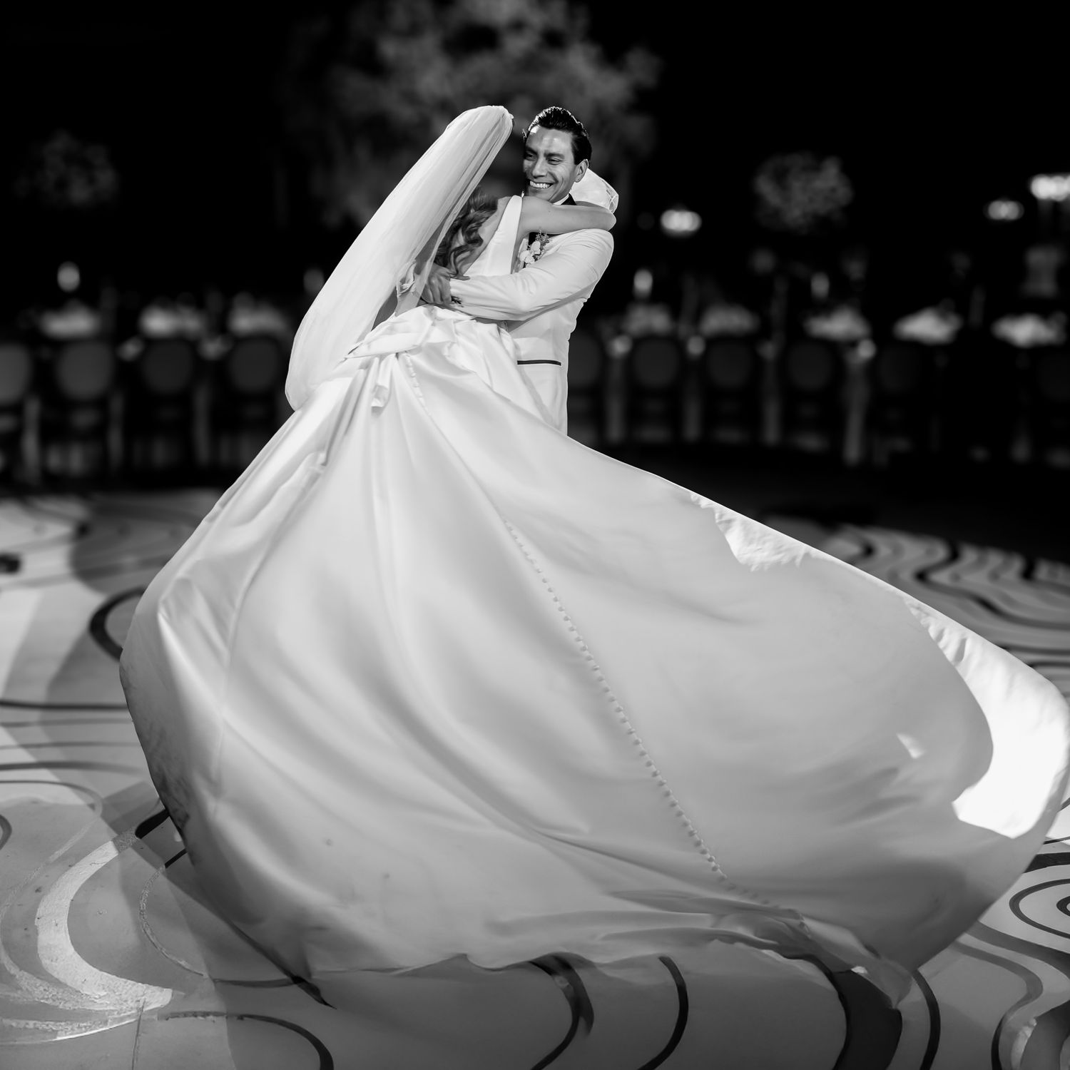 A black and white wedding photo captures a dramatic dance dip with flowing dress.