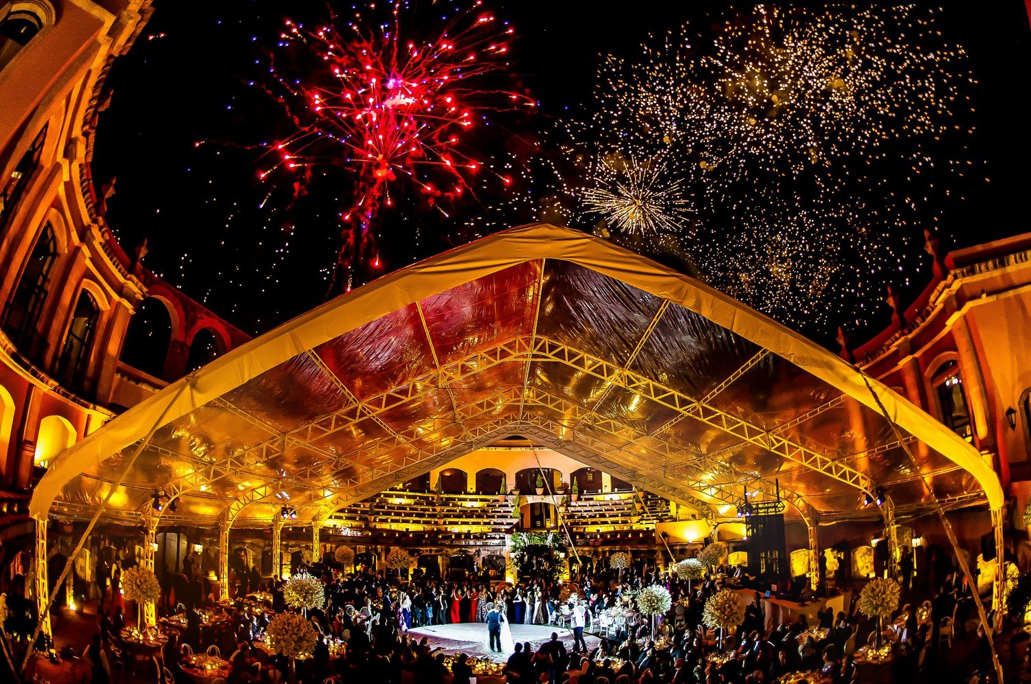 Red fireworks and sparklers illuminate an elegant wedding venue with dramatic lighting effects.