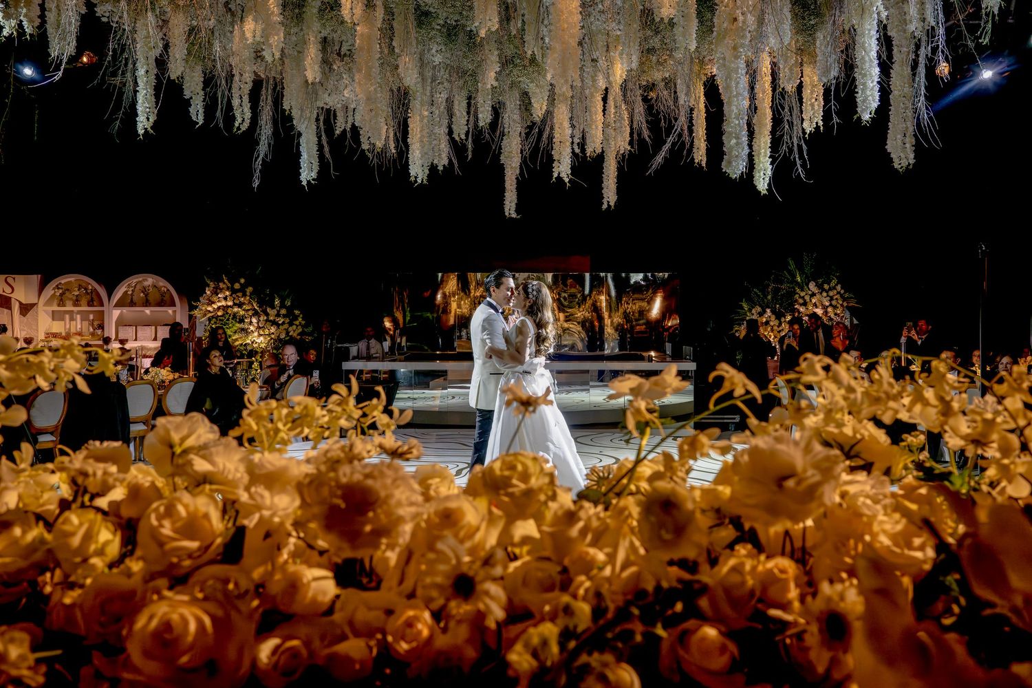 Wedding reception venue decorated with hanging floral installations and warm ambient lighting.