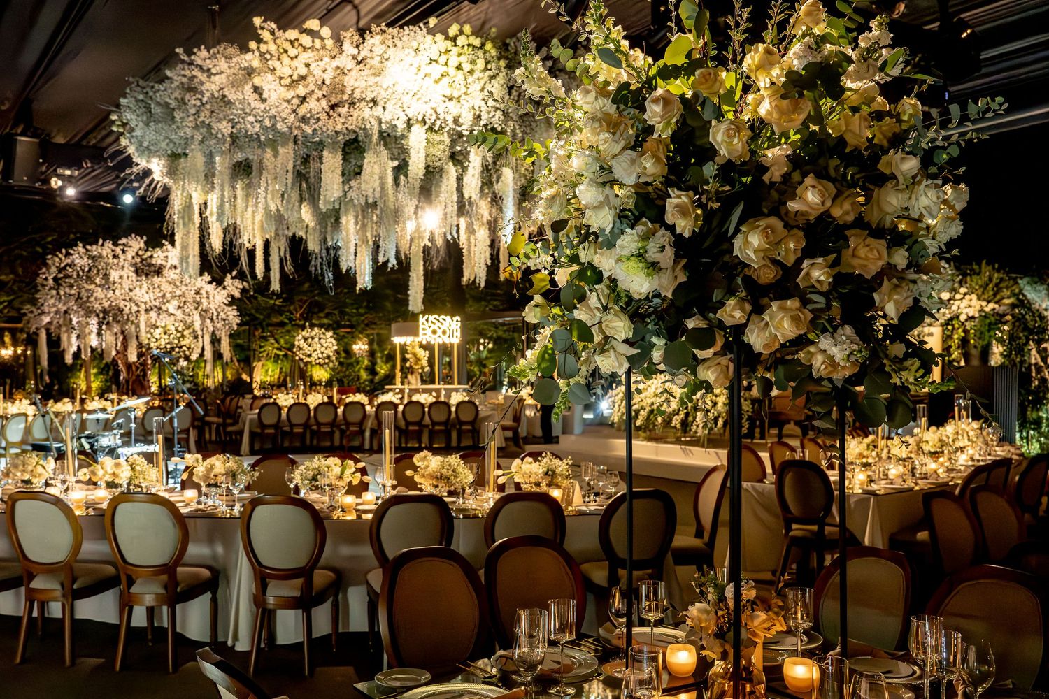 Wedding reception hall decorated with hanging fabric, crystal chandeliers, and vintage-style chairs.