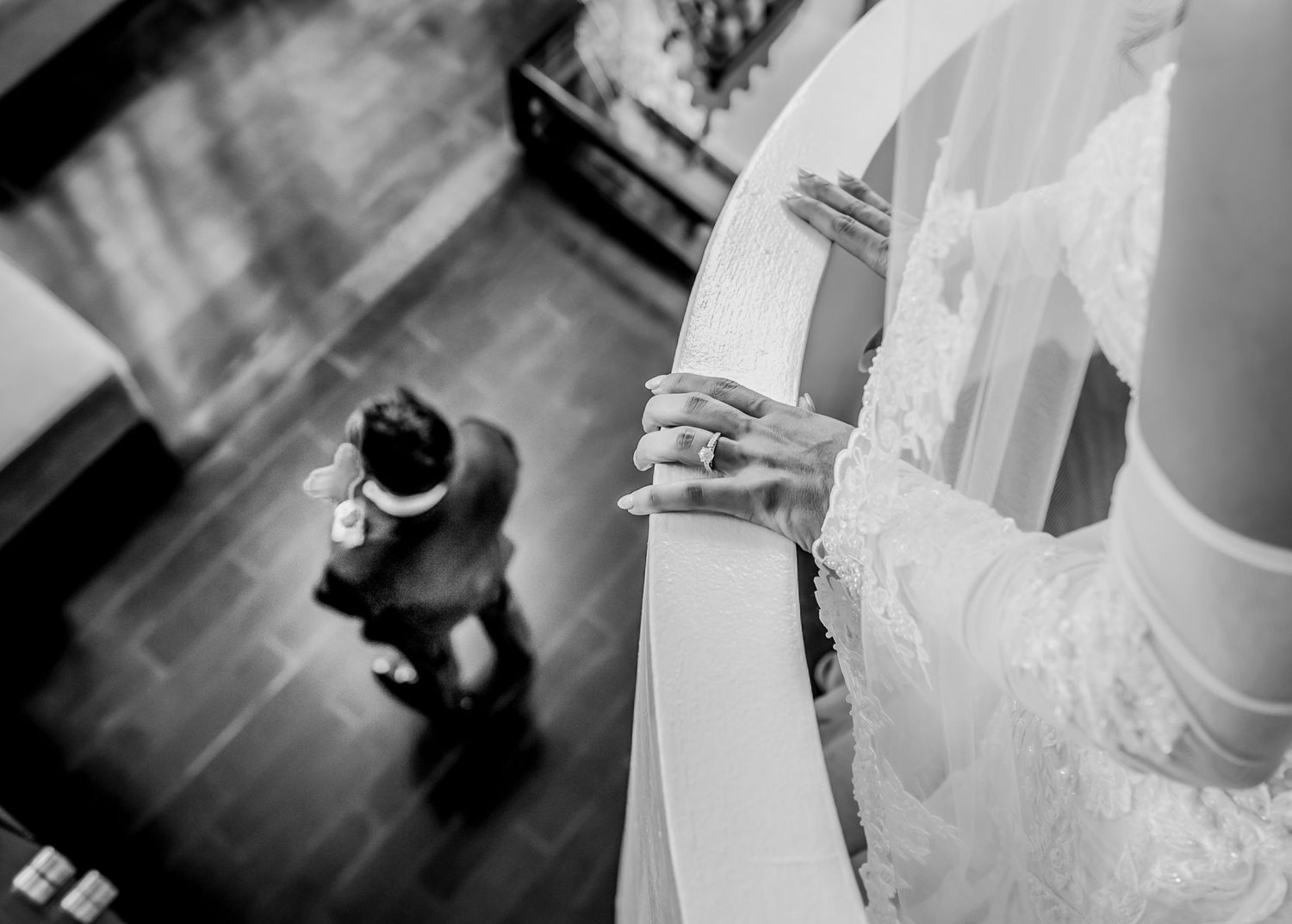 Black and white photo of a bride in an elegant wedding dress on a curved staircase.