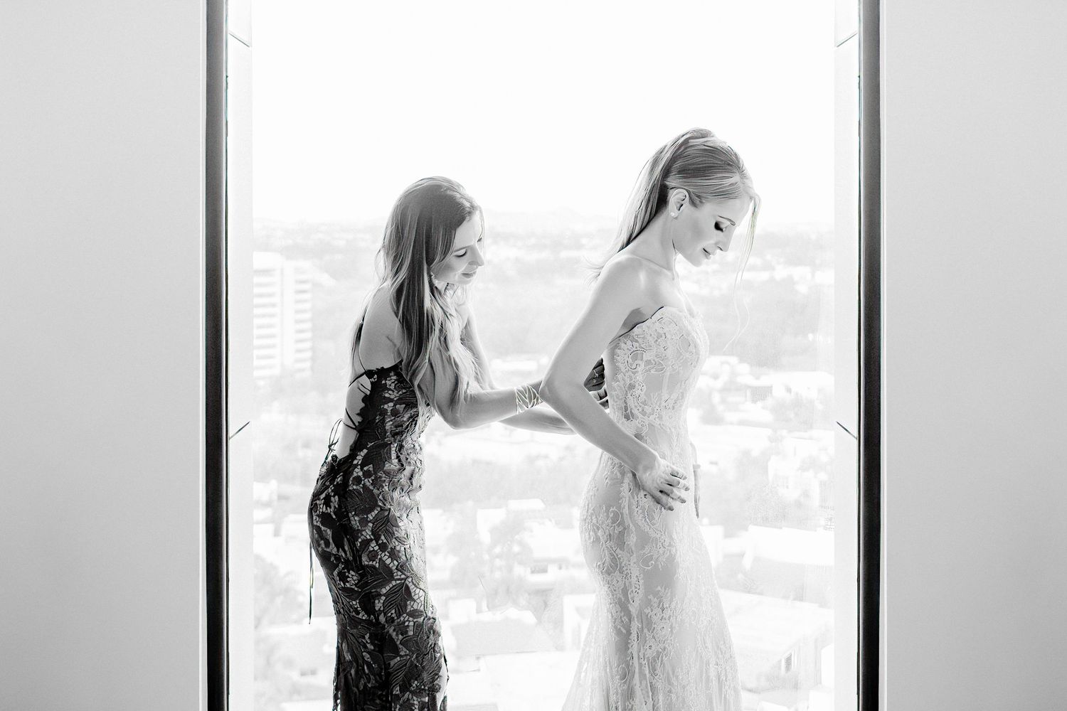 Black and white image of two figures in formal wear silhouetted against bright window.