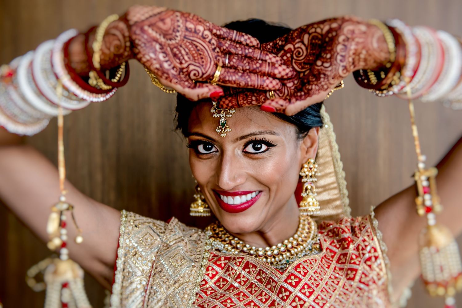 Indian bride in red bridal saree with intricate mehndi henna hands raised, wearing gold jewelry and tikka for wedding.
