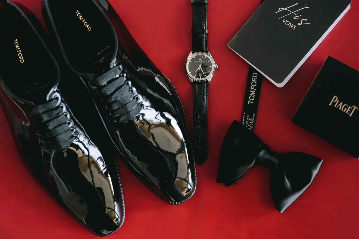 Black leather dress shoes and wallets arranged in a diagonal line against a red background.