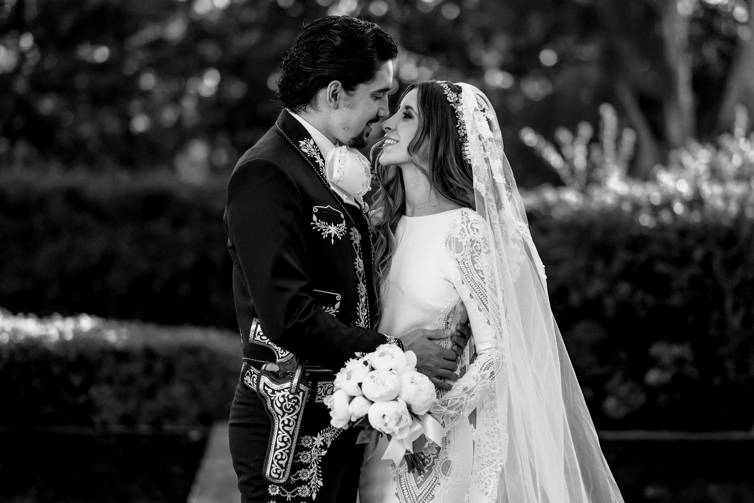 Black and white wedding photo of bride and groom sharing a romantic kiss outdoors, bride holding bouquet.