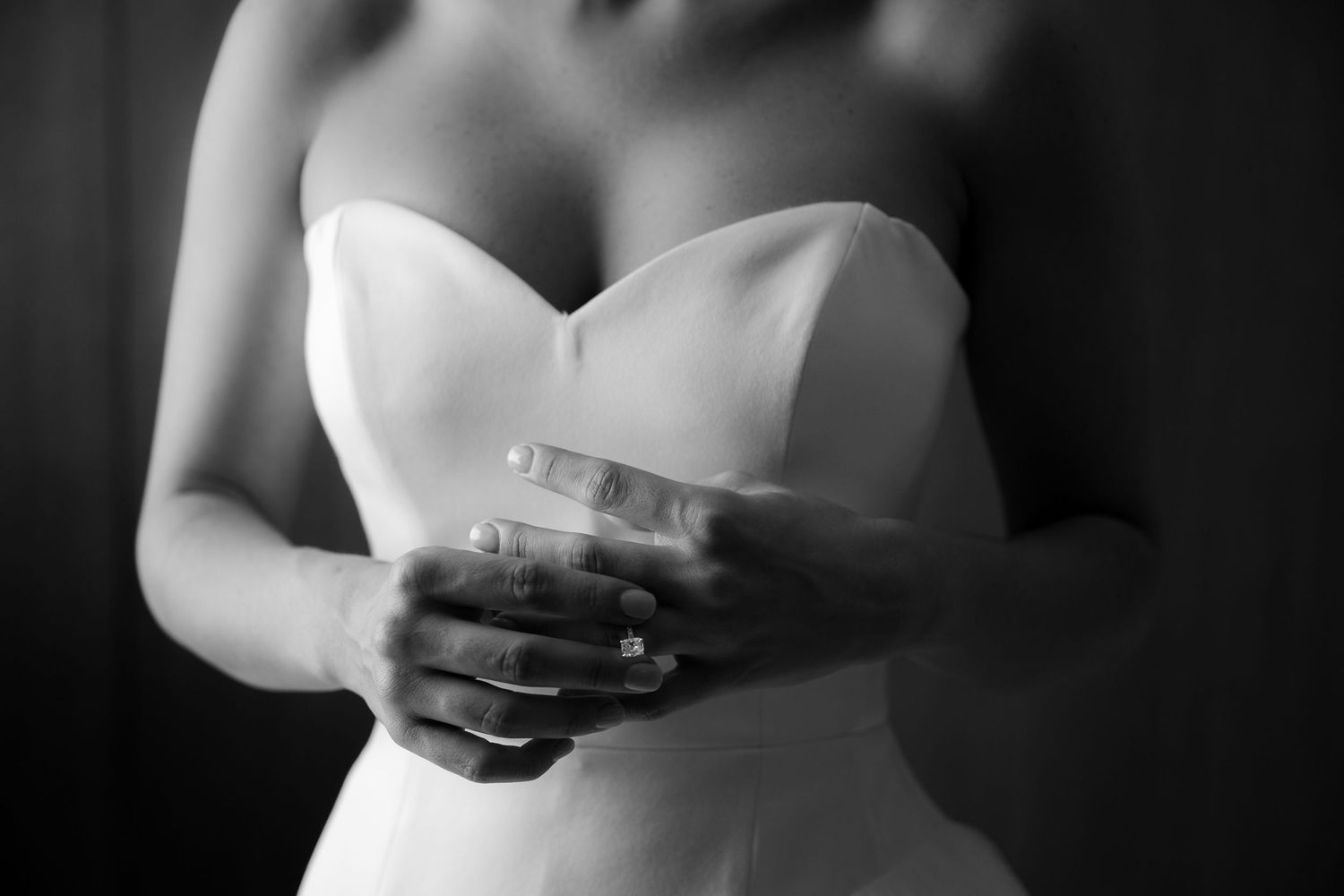 Black and white photo of a bride in a strapless wedding gown clasping her hands together, showcasing her engagement ring.