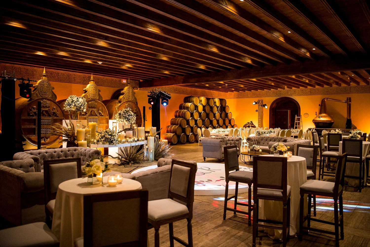 Elegant winery event venue with warm lighting, barrel walls, draped tables, and upscale seating for a sophisticated dining experience.