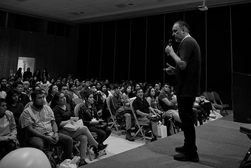 Wide shot of darkened auditorium with audience members attending a photography presentation.