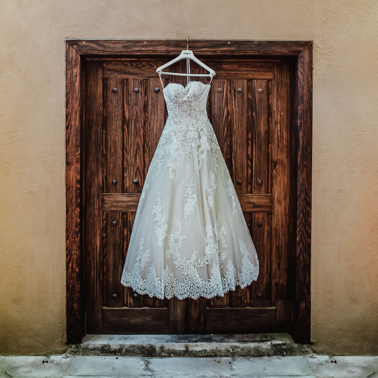 A delicate lace wedding dress hanging on wooden door creating artistic contrast.