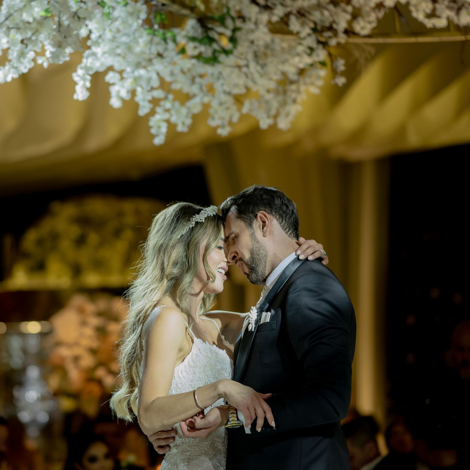 A romantic wedding moment under delicate white floral decorations with golden lighting.
