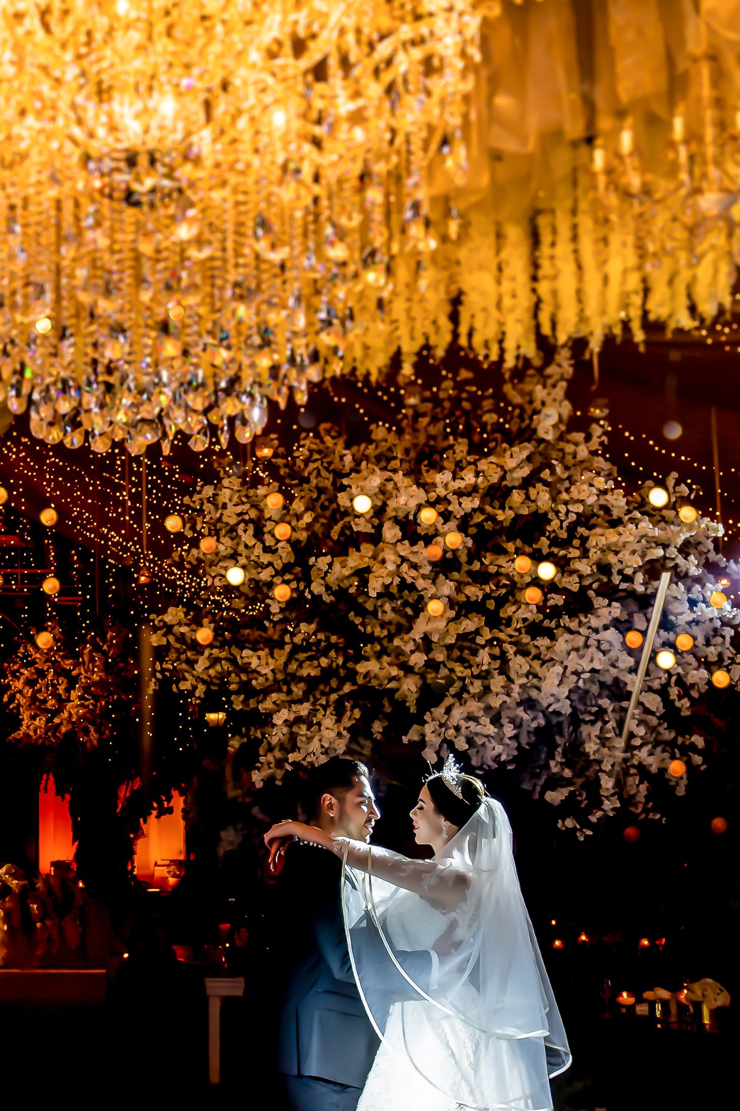 Elegant wedding reception featuring cascading crystal chandeliers and warm amber lighting.