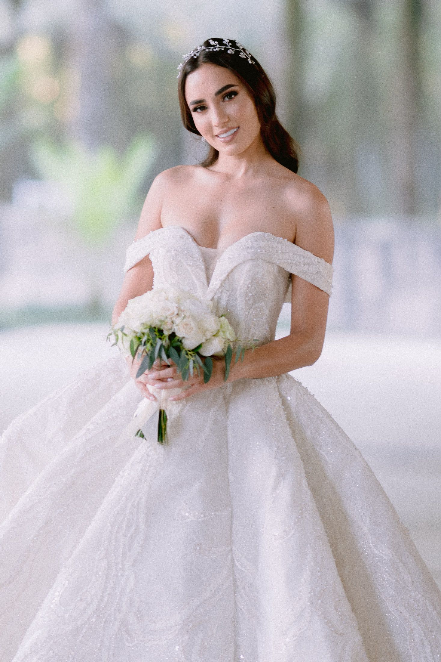 Off-shoulder bridal gown with delicate lace details and white bouquet in natural lighting.