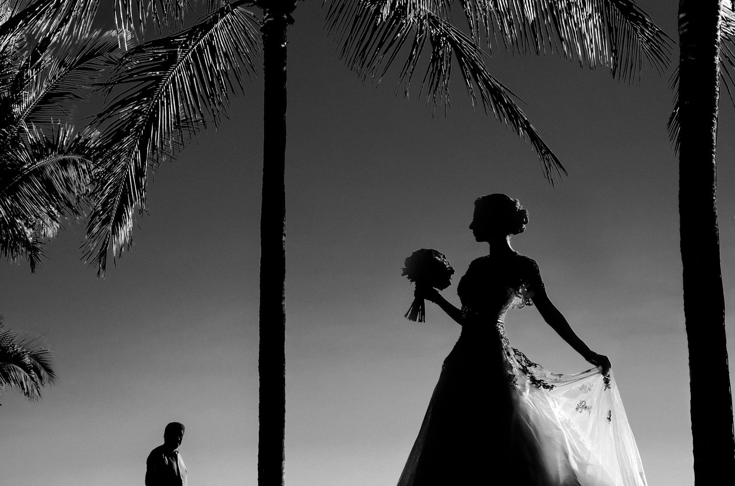Silhouetted couple walking along a beach at sunset with palm trees framing the romantic scene.
