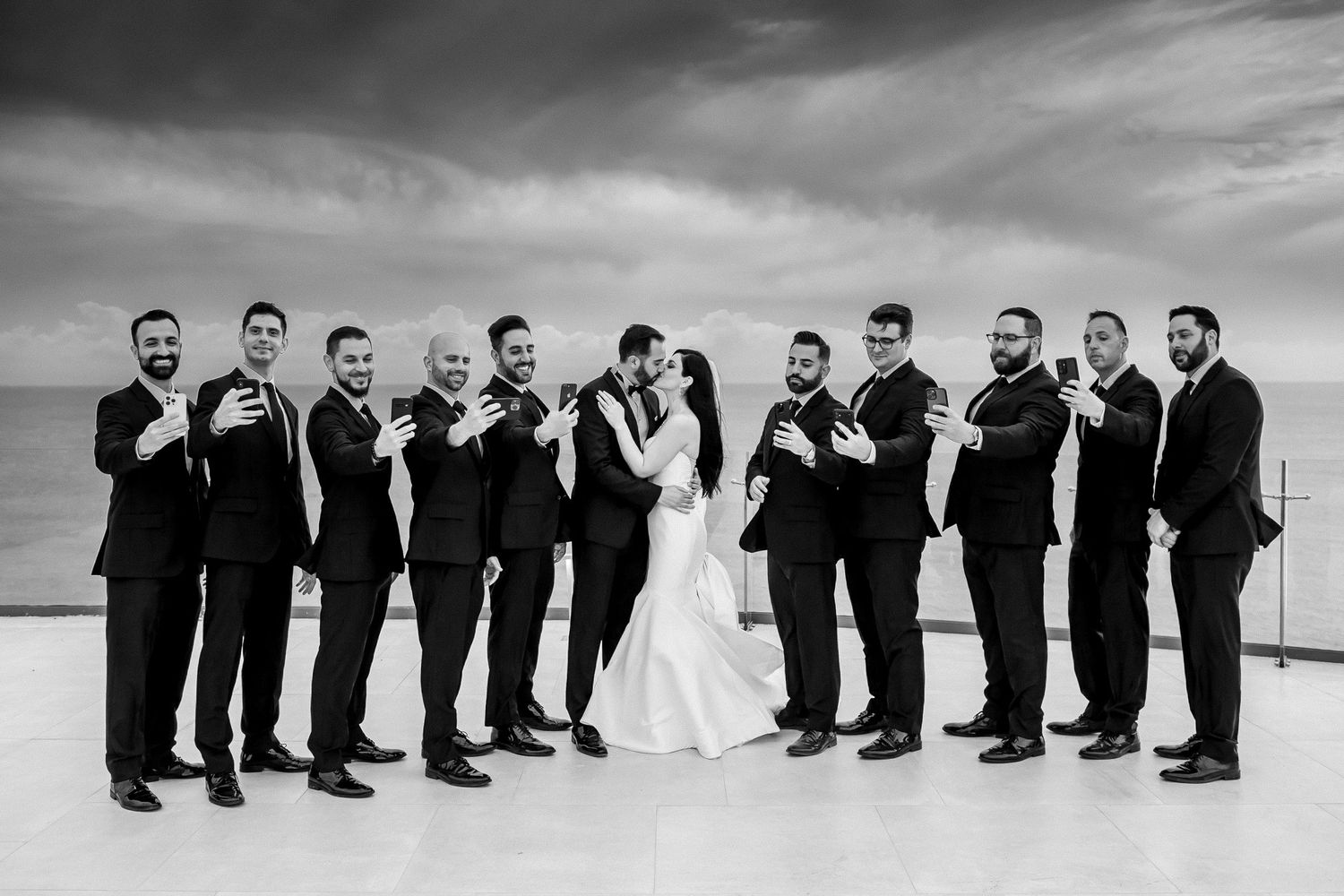 Black and white panoramic shot of wedding party lined up against dramatic sky.