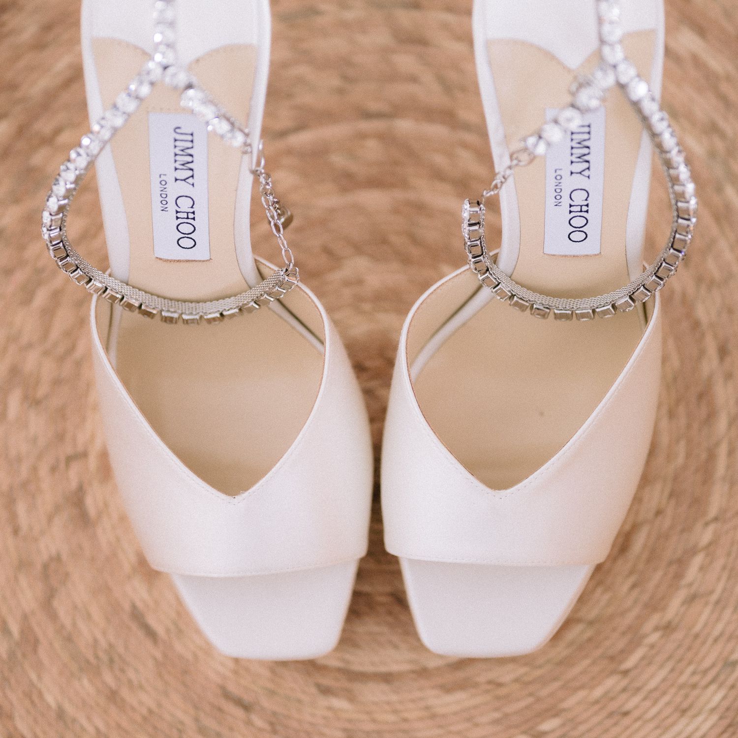 White Jimmy Choo bridal shoes with crystal embellishments on woven texture background.