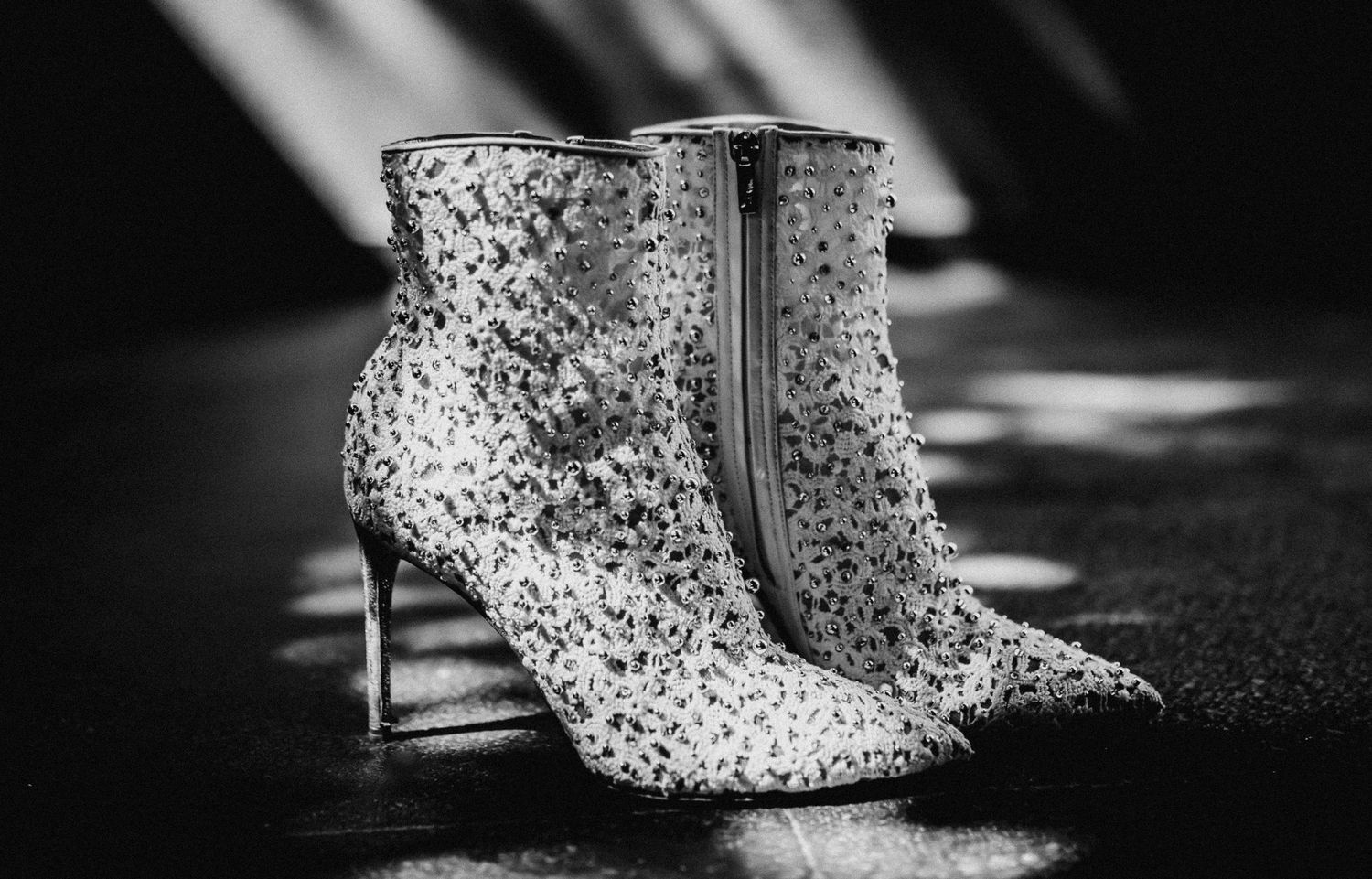 Black and white photo of sparkly sequined stiletto ankle boots with side zipper on dark reflective surface.
