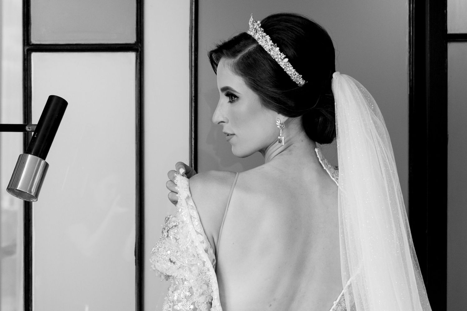 Black and white photo of a bride in a lace gown and tiara, showing her elegant back detail with veil.