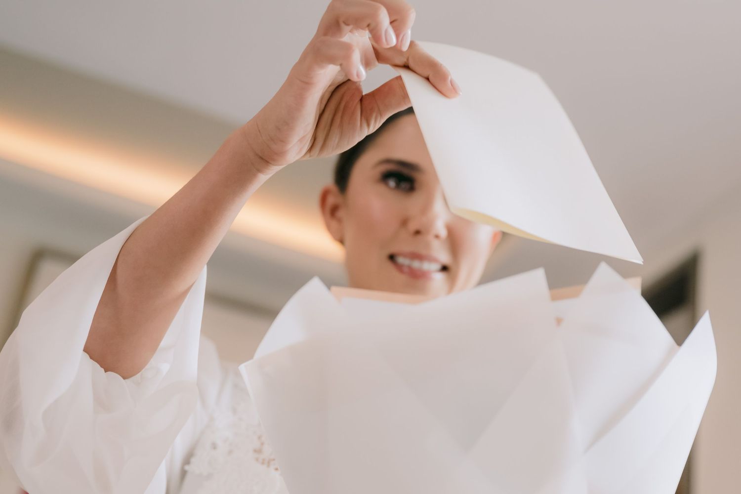 A bride in a white gown holds up her wedding veil, preparing to put it on before her ceremony.