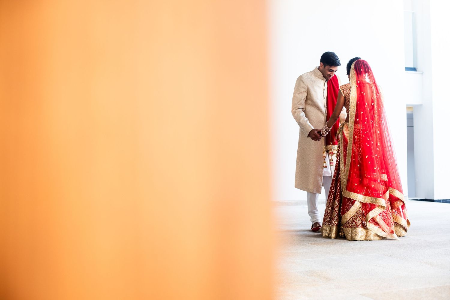 Indian bride in red lehenga and groom in gold sherwani share an intimate moment during traditional wedding ceremony.