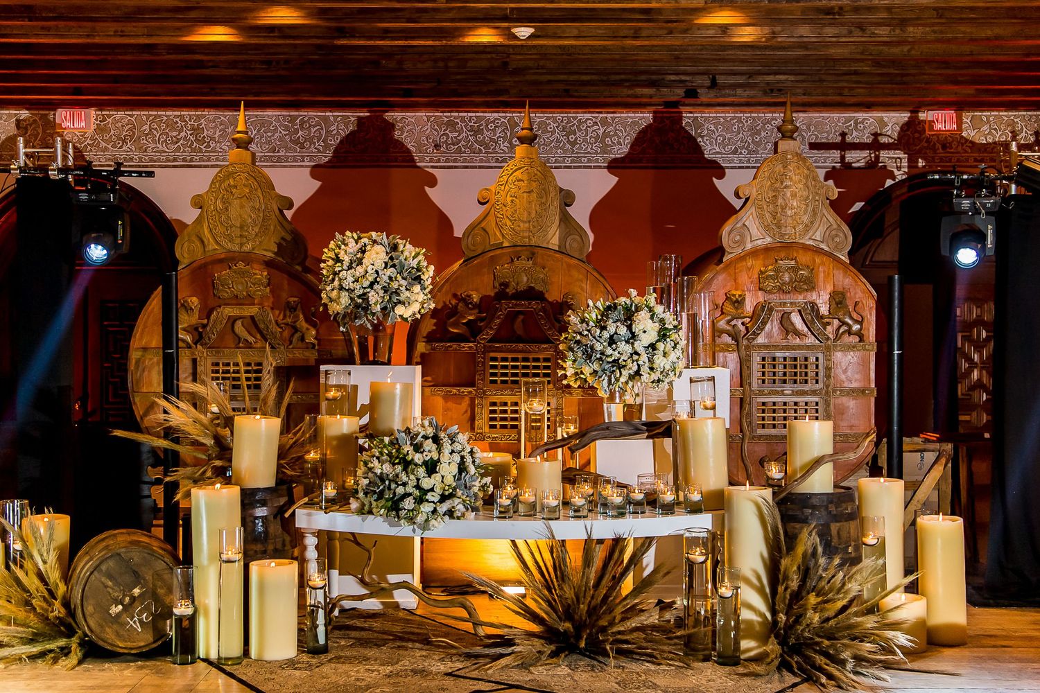 Elegant wedding sweetheart table with candles, floral arrangements, and ornate golden backdrop decor.