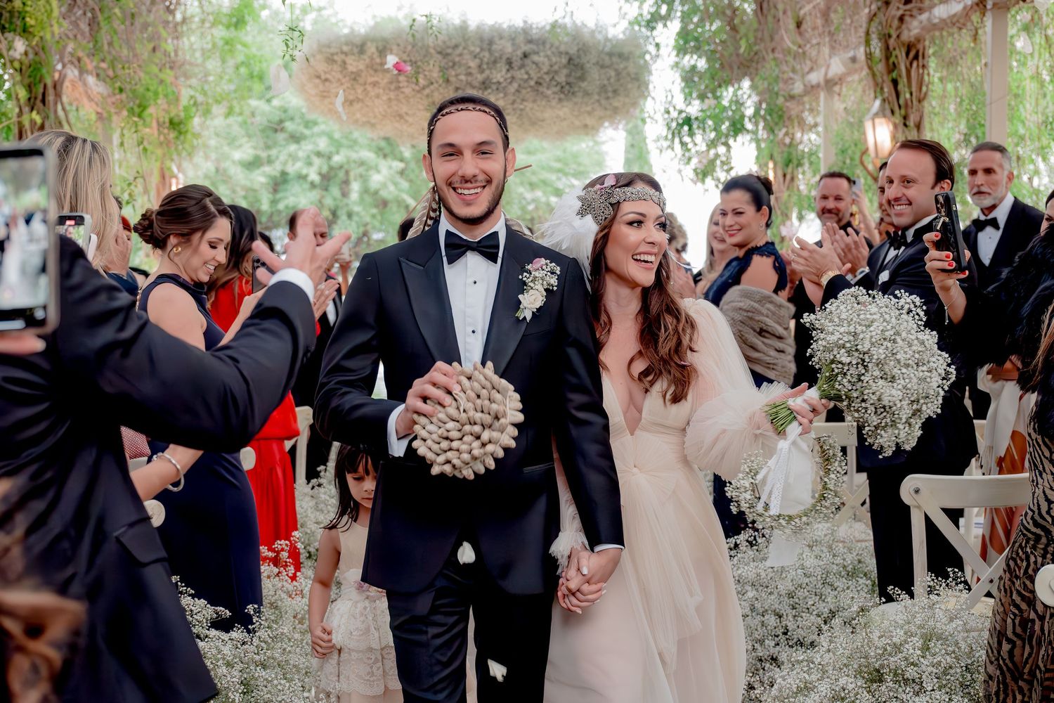 Bride and groom walk down the aisle smiling, surrounded by cheering guests in an elegant outdoor wedding ceremony.