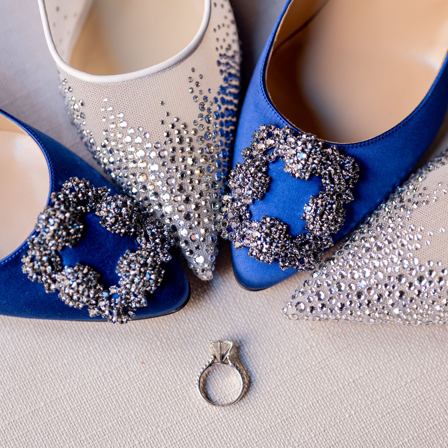 Blue crystal-embellished wedding shoes displayed with engagement ring on light background.