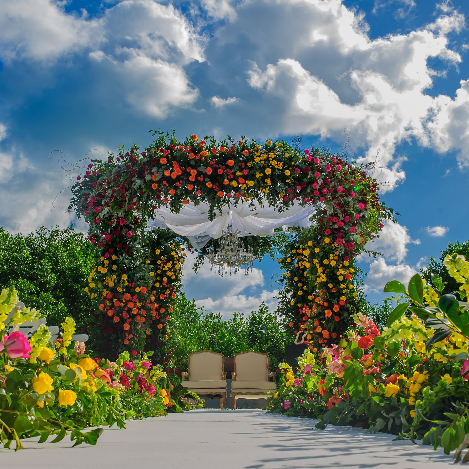 Beautiful floral arch with vibrant roses and tropical flowers against a bright blue sky.