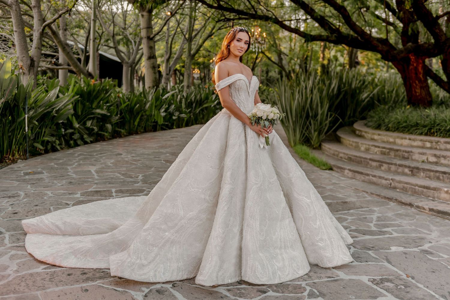 Luxurious off-shoulder wedding gown with textured skirt photographed in garden setting.
