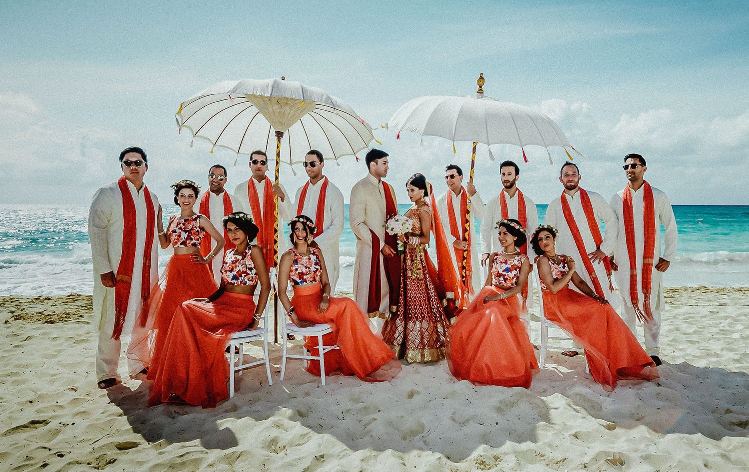 Beach wedding party with bridesmaids in coral dresses and groomsmen in light suits.