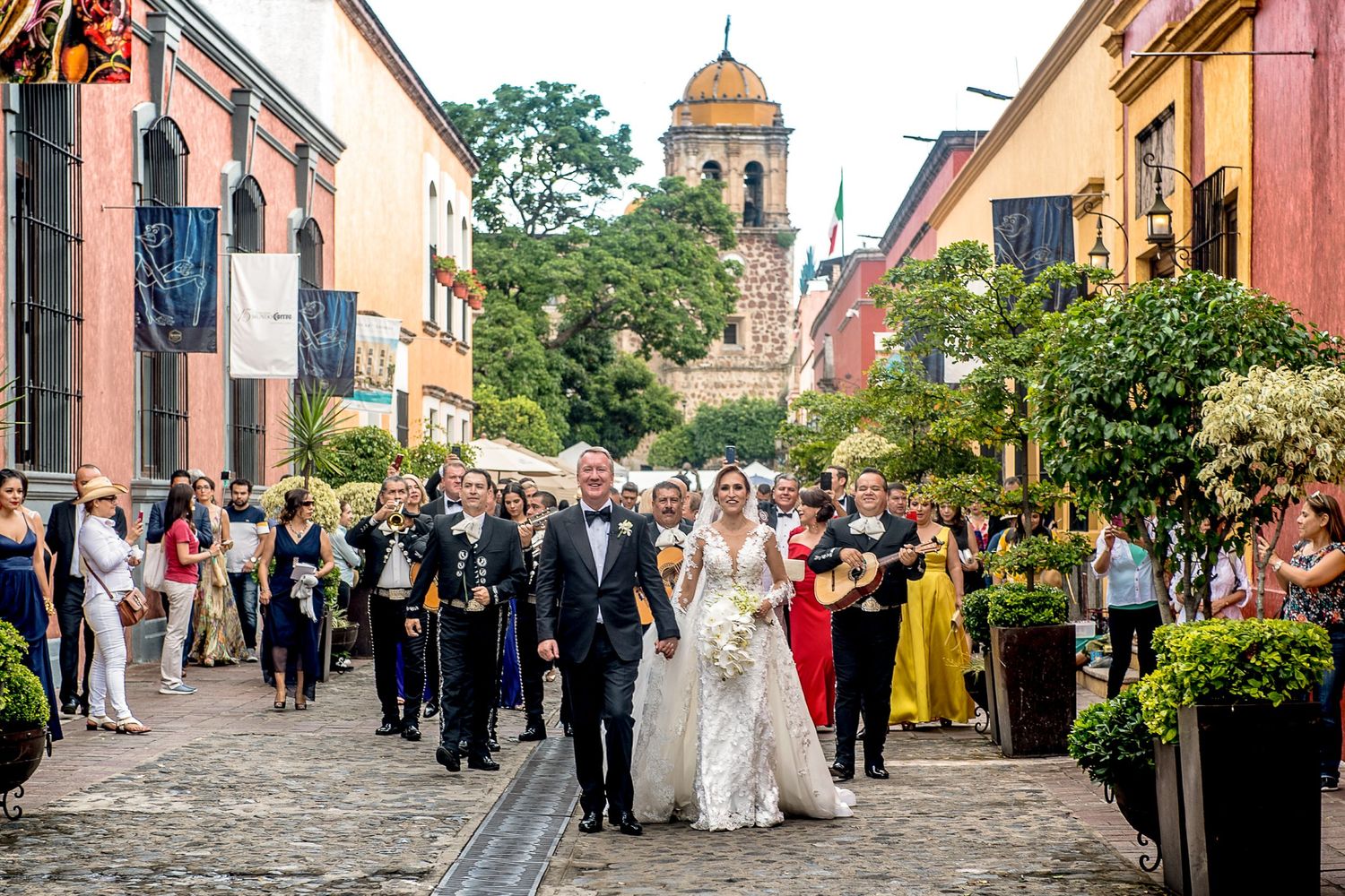 Bride walks down cobblestone street with wedding party in San Miguel de Allende, Mexico, church visible in background.