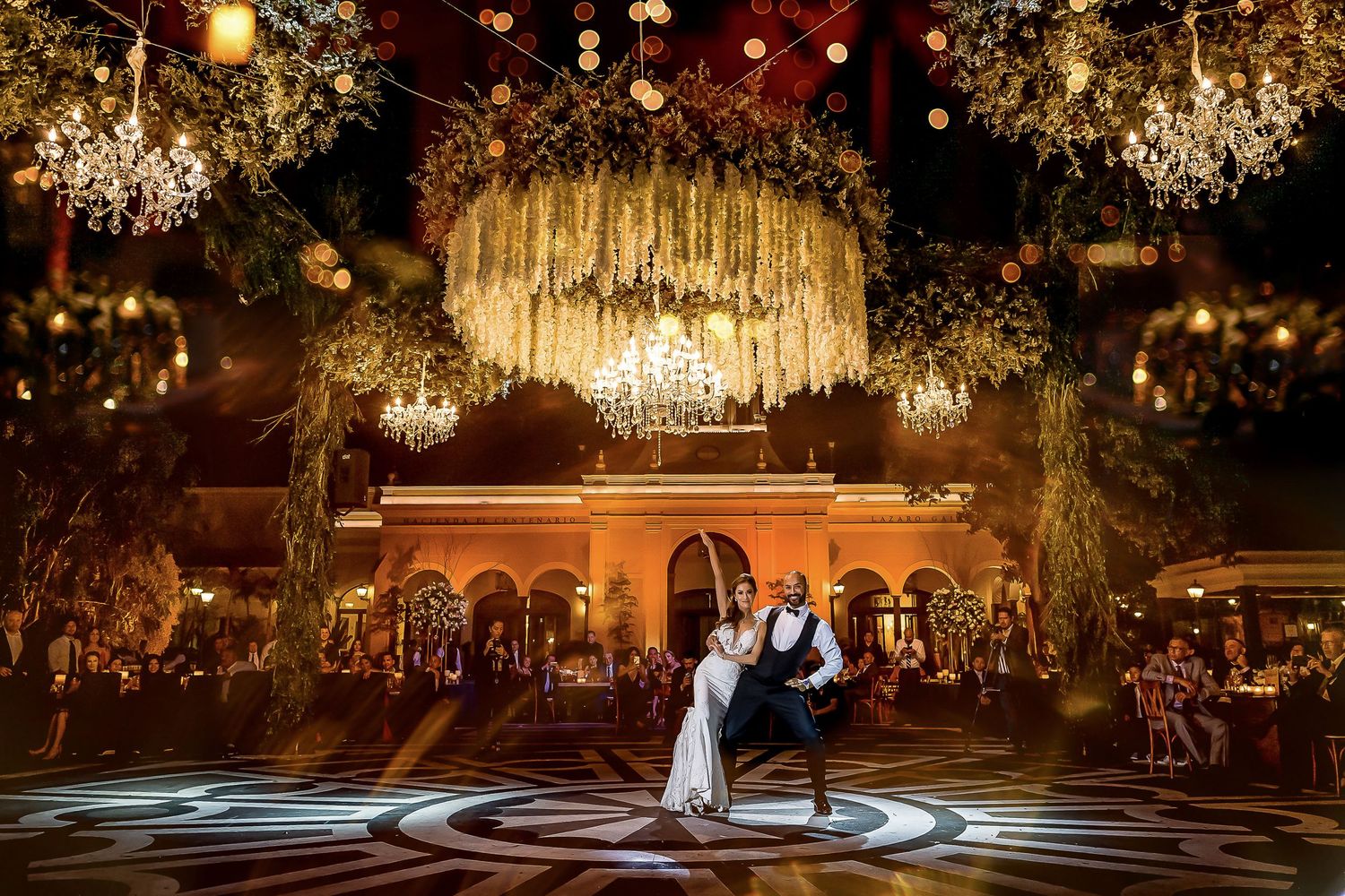 Bride and groom share first dance under floral chandelier at elegant outdoor wedding reception.