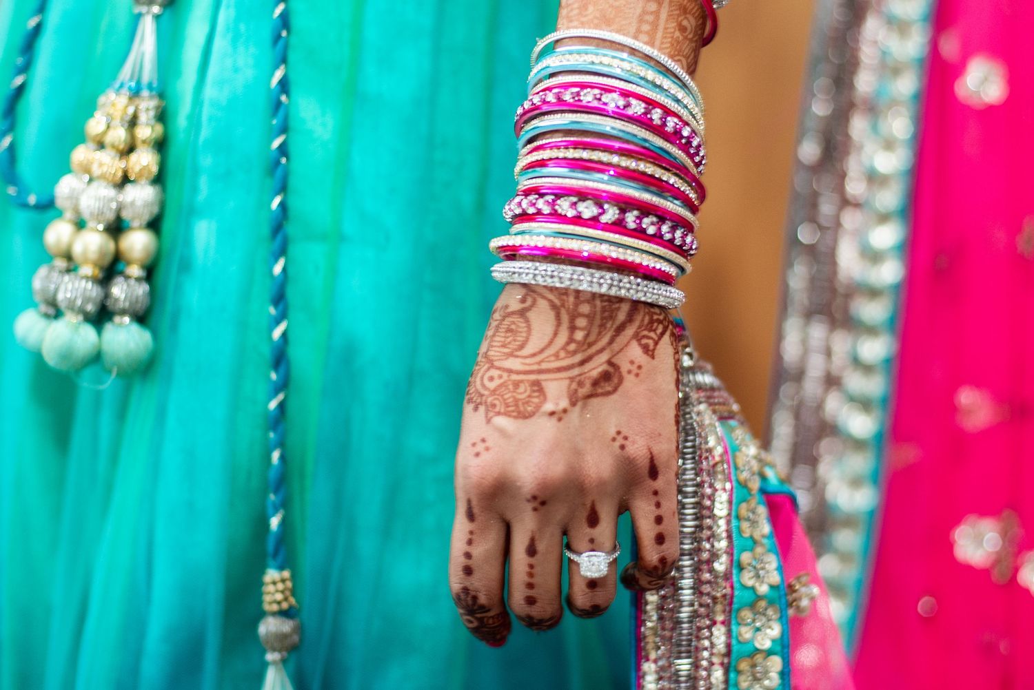 Close-up of a bride's hand adorned with henna mehndi, colorful bangles, and a diamond ring at an Indian wedding.