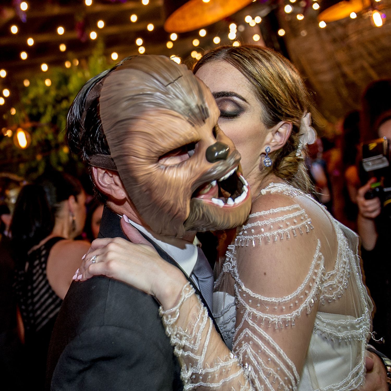 Romantic couple sharing intimate moments under warm glowing lights at an evening celebration.