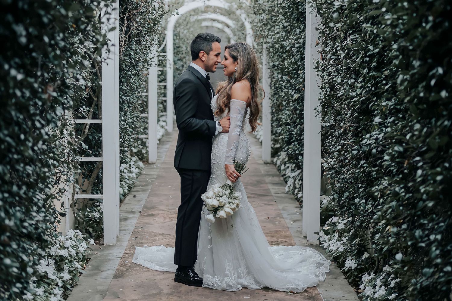 Intimate wedding portraits captured in a garden archway with ivy and white columns.