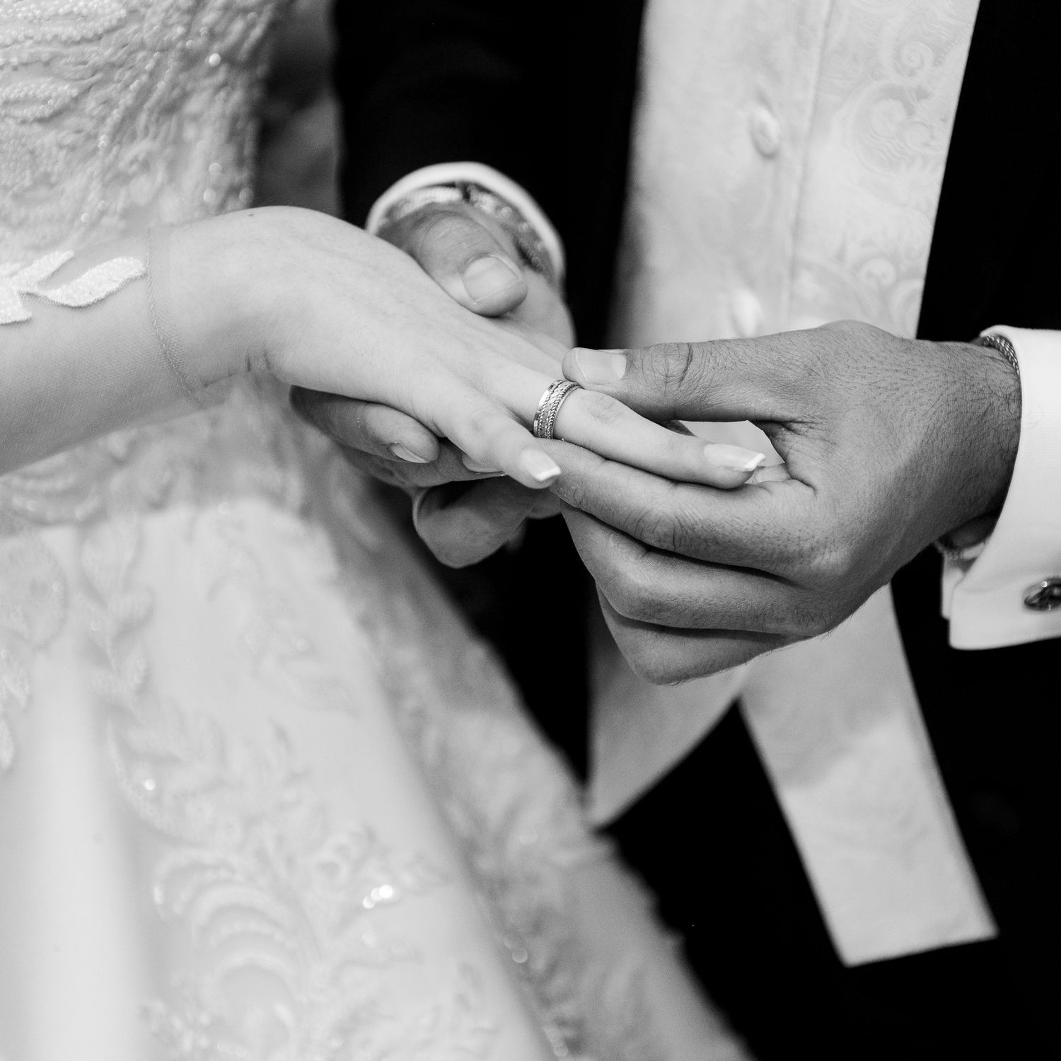 Intimate moment of ring exchange during wedding ceremony captured in black and white.