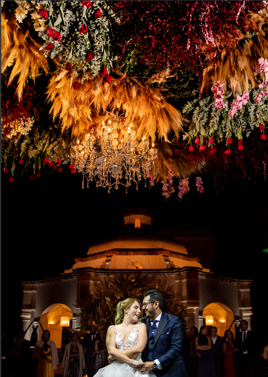 Wedding reception venue with dramatic floral ceiling installation and crystal chandelier.