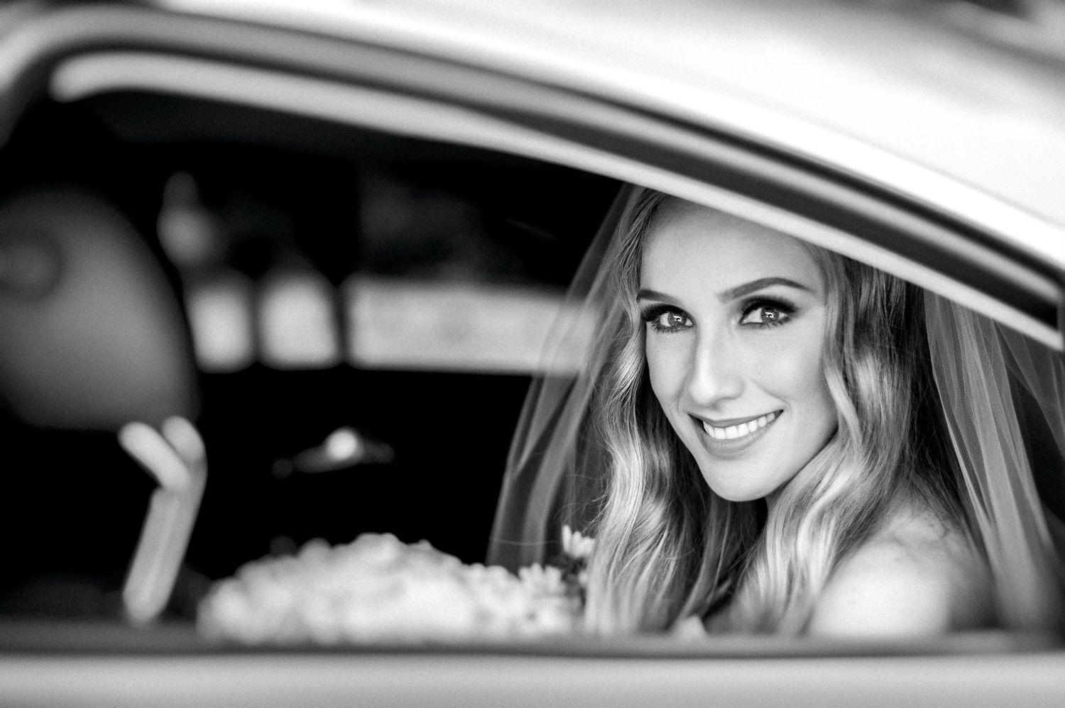 Black and white portrait of a smiling passenger looking through a car window with a joyful expression.