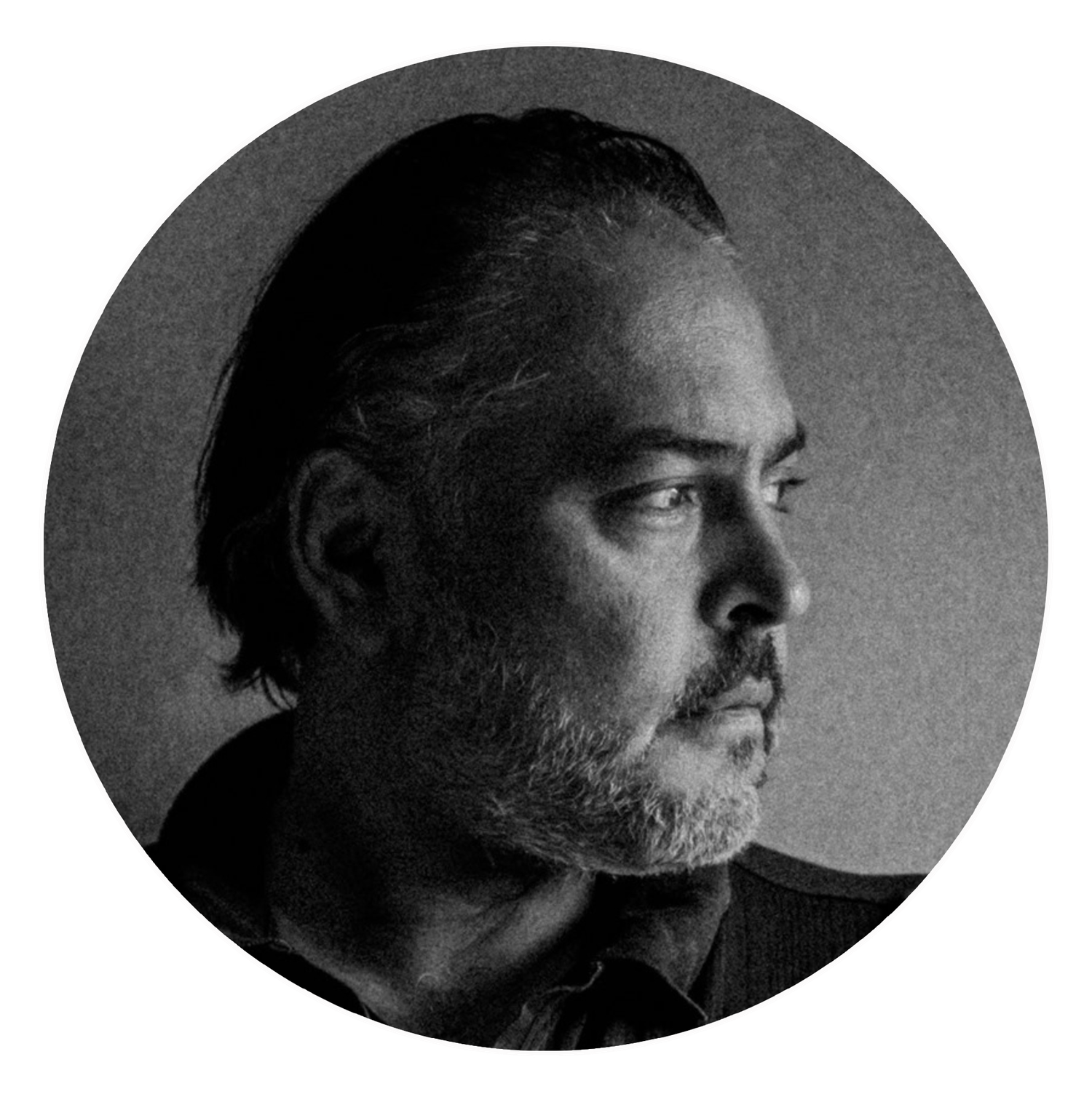 Black and white profile portrait of a bearded man in dramatic side lighting against a dark background.